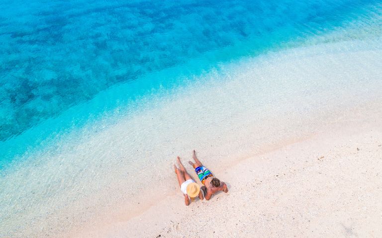 Aerial shot of a couple sunbathing on the white sand beaches of Vanuatu