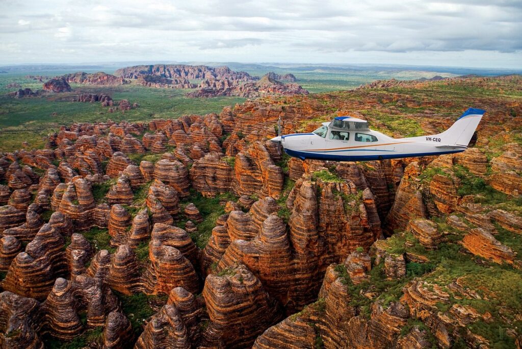 Aerial shot of a small plane flying over the red striped Bungle Bungle range