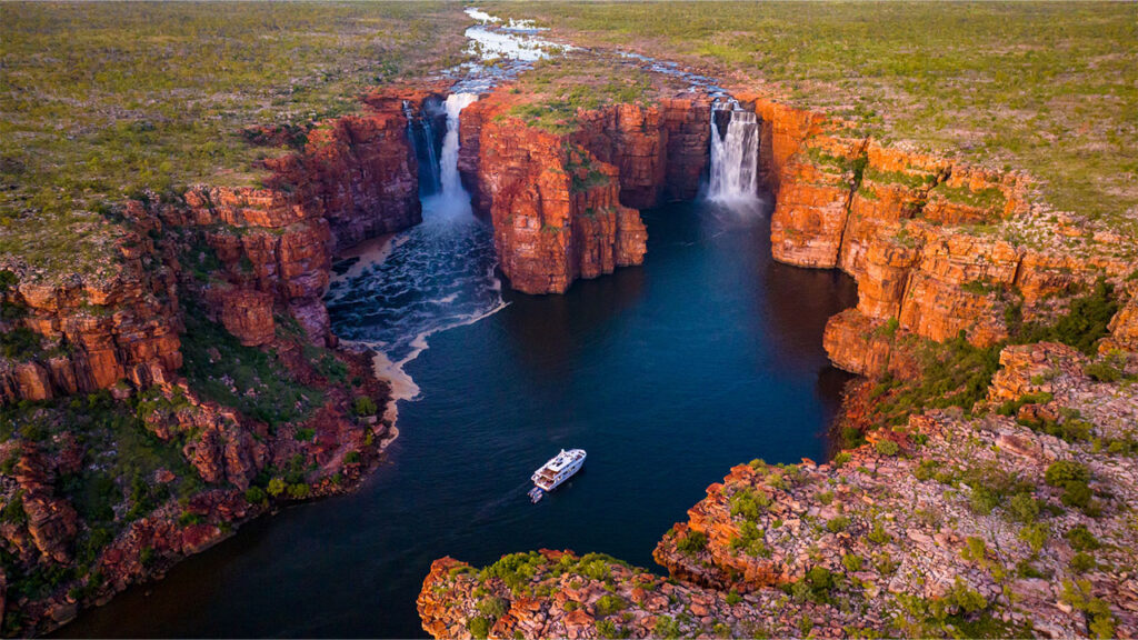 Aerial shot of a cruise ship in the Kimberley surrounded by cliffs and two waterfalls