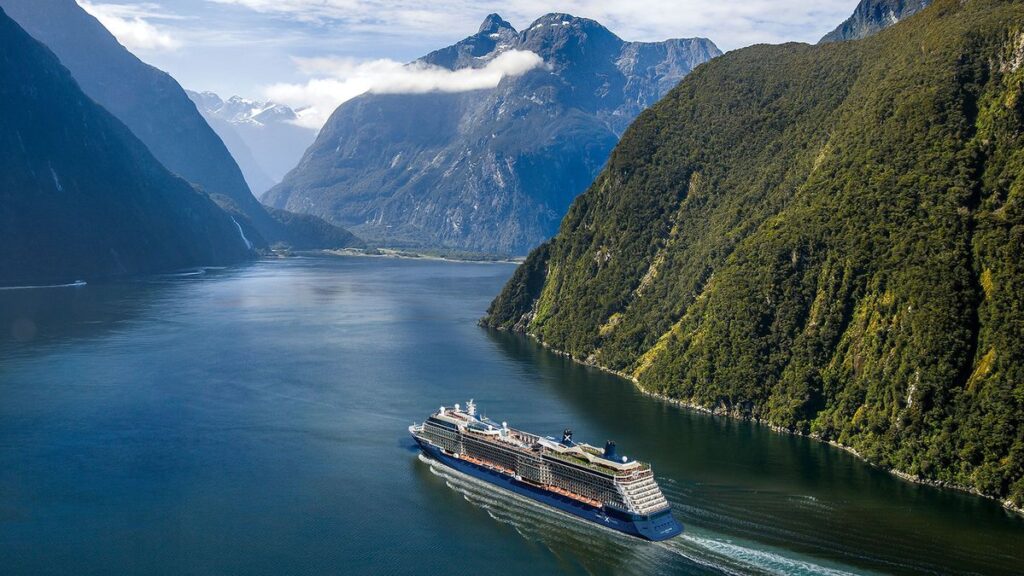 Aerial shot of a cruise ship travelling through the coastal mountain range of Milford Sound in New Zealand